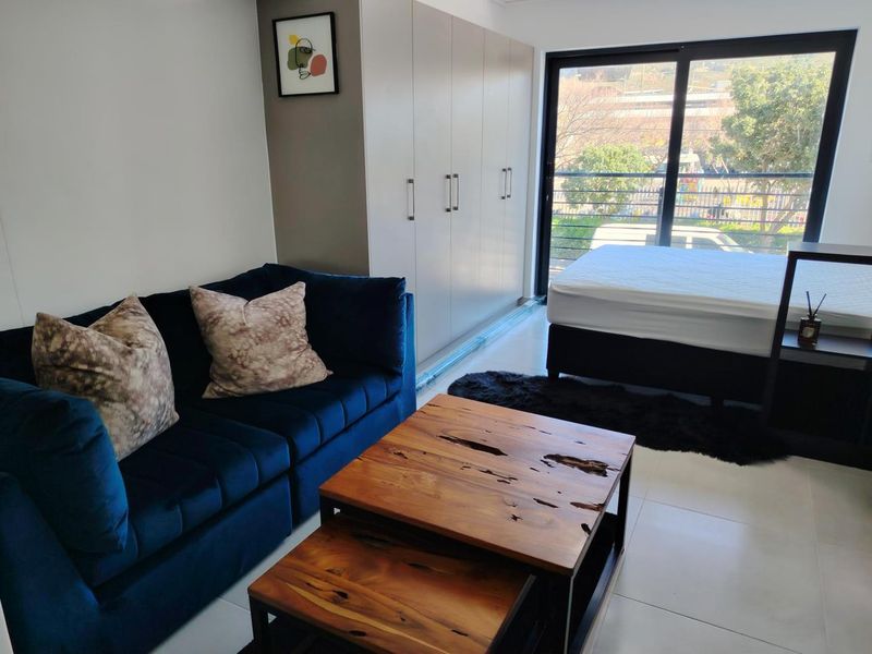 A modern open-plan living and sleeping area featuring neutral tiled flooring, ample built-in cupboard storage, and large sliding glass doors leading to a balcony.