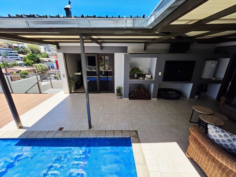 Covered outdoor patio featuring a built-in braai area, tiled flooring, and direct access to a swimming pool.