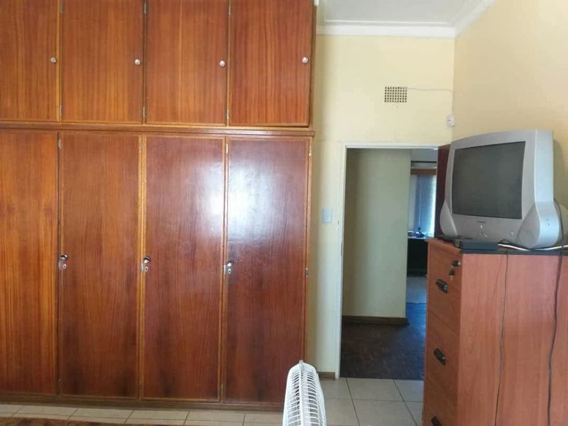 Bedroom featuring extensive floor-to-ceiling built-in wooden cupboards and tiled flooring, offering ample storage space in a dated interior setting.