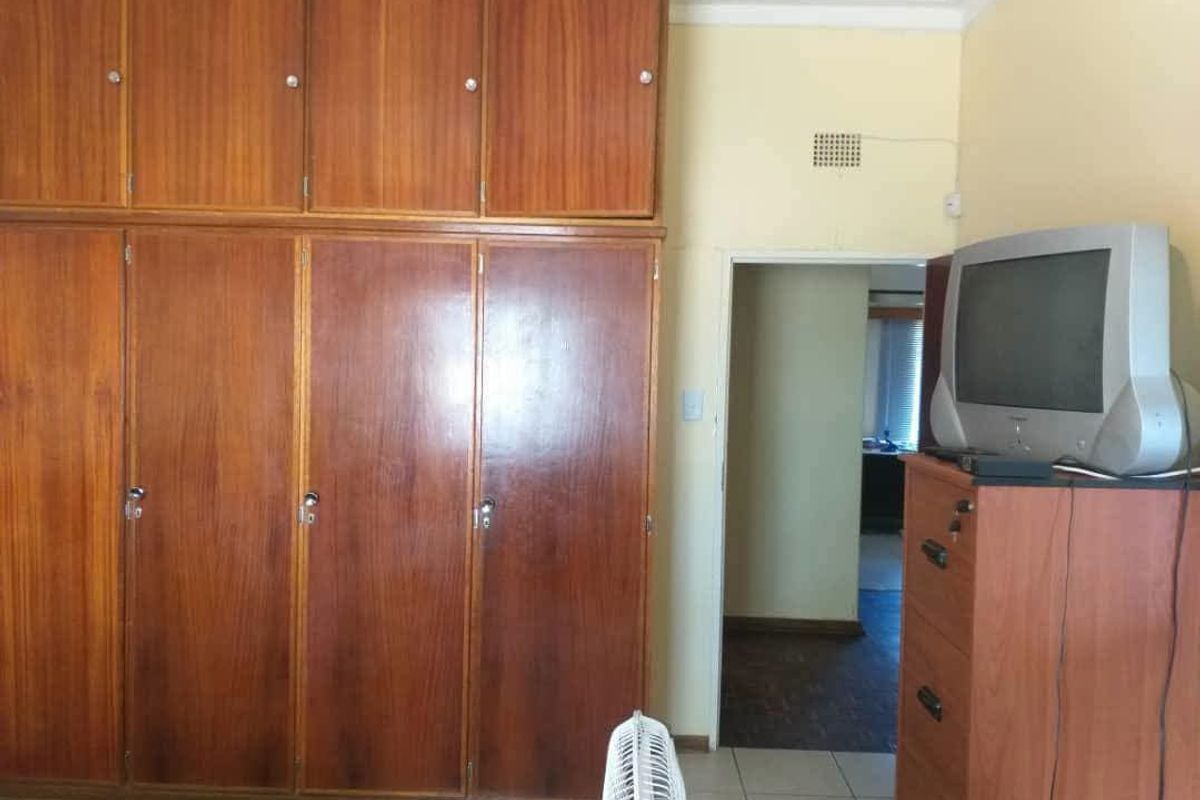 Bedroom featuring extensive floor-to-ceiling built-in wooden cupboards and tiled flooring, offering ample storage space in a dated interior setting.
