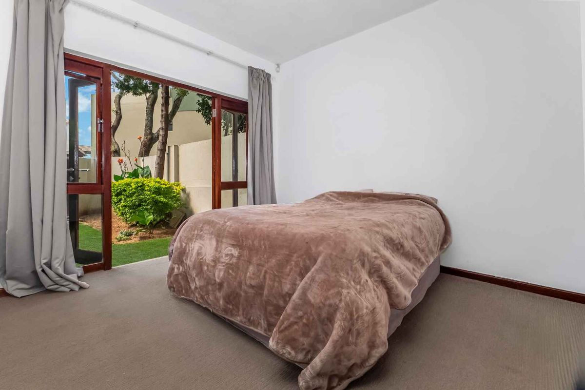 A bedroom featuring neutral carpeting and large timber-framed glass doors providing direct access to a private garden area.