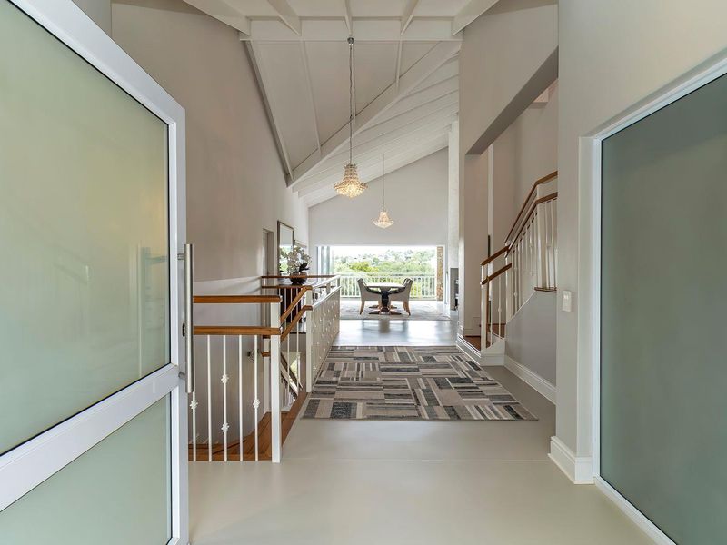 Spacious entrance hall featuring high vaulted ceilings, elegant pendant lighting, and a staircase with timber handrails, leading towards an open-plan living area with scenic views.