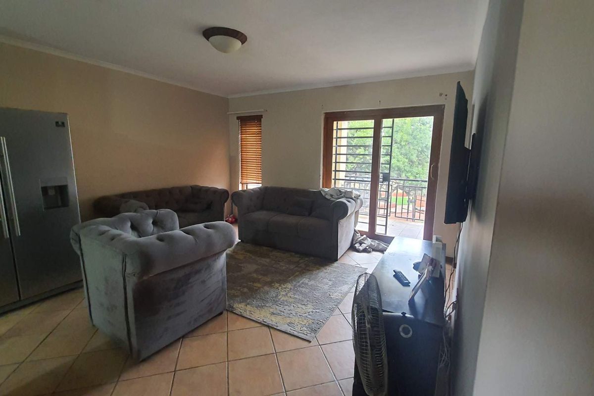 A living room featuring tiled flooring, a sliding glass door with security gate, and access to an outdoor balcony area.