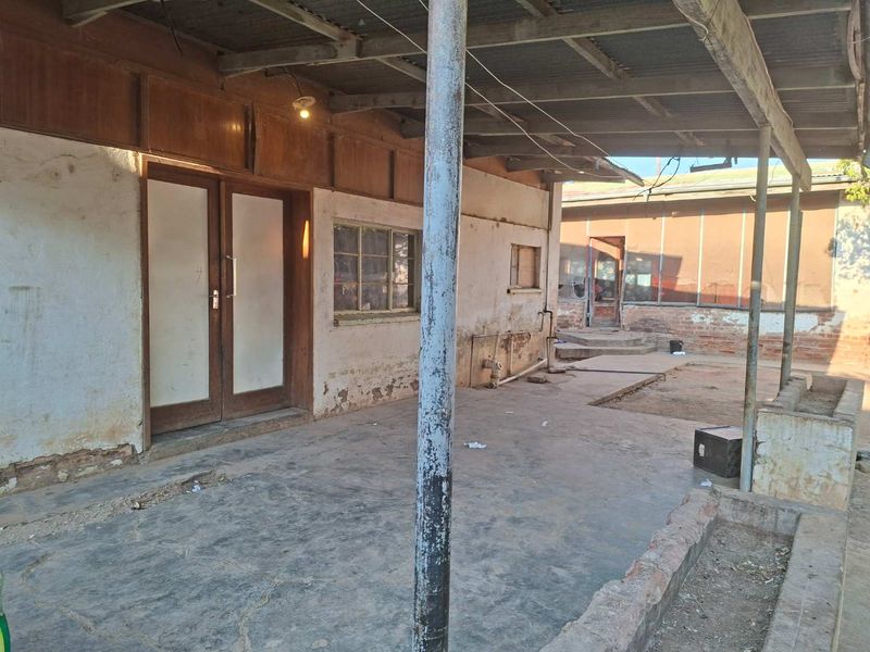 A covered outdoor patio area featuring a corrugated metal roof, steel support columns, and a brick planter box, requiring significant maintenance and cosmetic restoration.