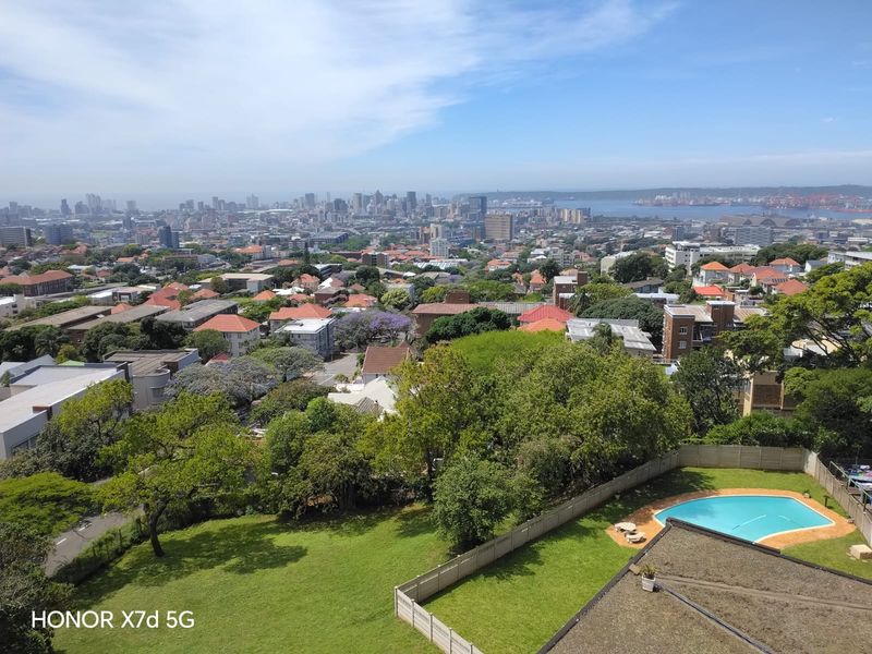 Elevated panoramic city and coastal view overlooking a residential area with a private swimming pool and garden.