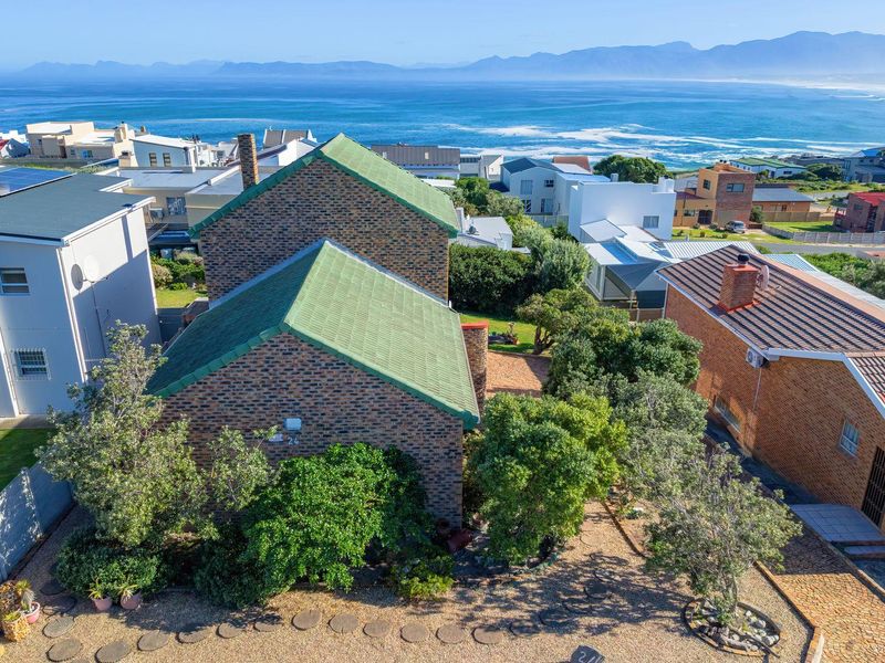 Aerial view of a brick residential property featuring a pitched roof, chimney, and paved outdoor area, set against a scenic coastal and mountain backdrop.
