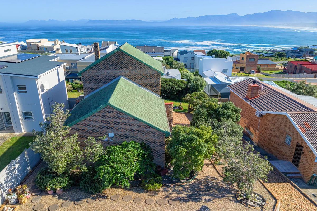 Aerial view of a brick residential property featuring a pitched roof, chimney, and paved outdoor area, set against a scenic coastal and mountain backdrop.
