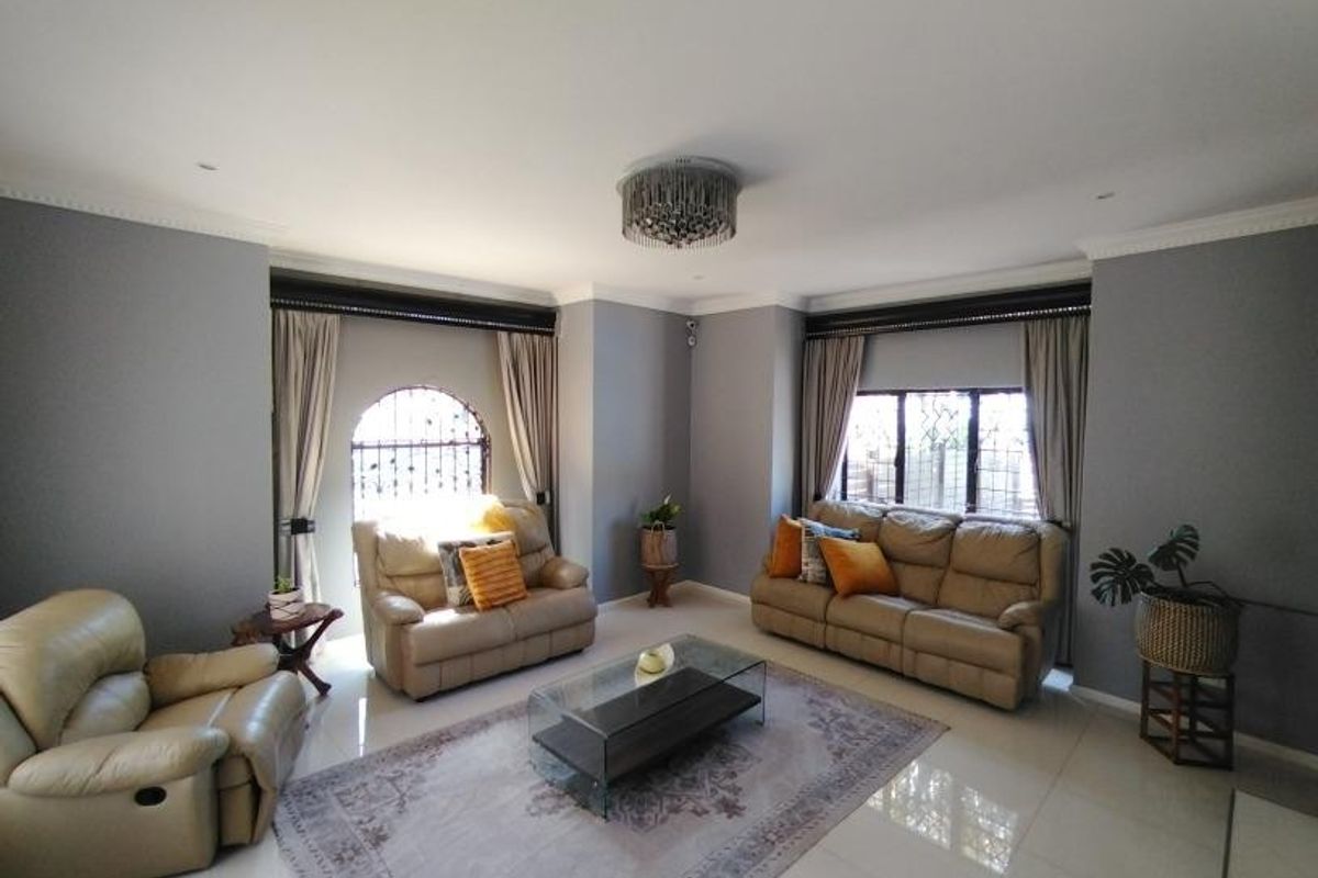Spacious living room featuring tiled flooring, crown molding, and large windows with security bars, providing a bright and well-maintained living space.
