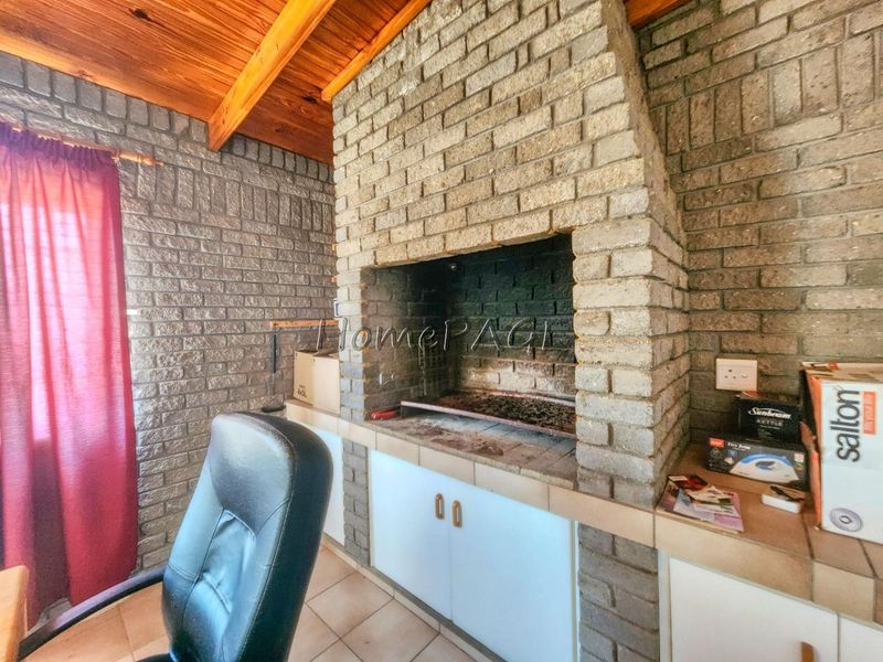 Covered patio area featuring a large built-in brick braai, exposed timber ceiling beams, and brick wall finishes, offering a rustic entertainment space.