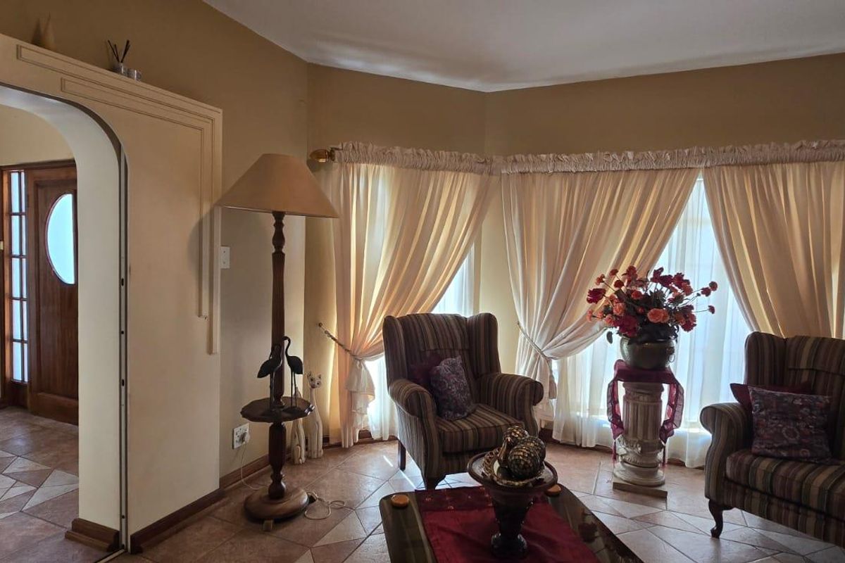 A cozy living room featuring tiled flooring, an arched doorway leading to the entrance, and large windows with draped curtains.