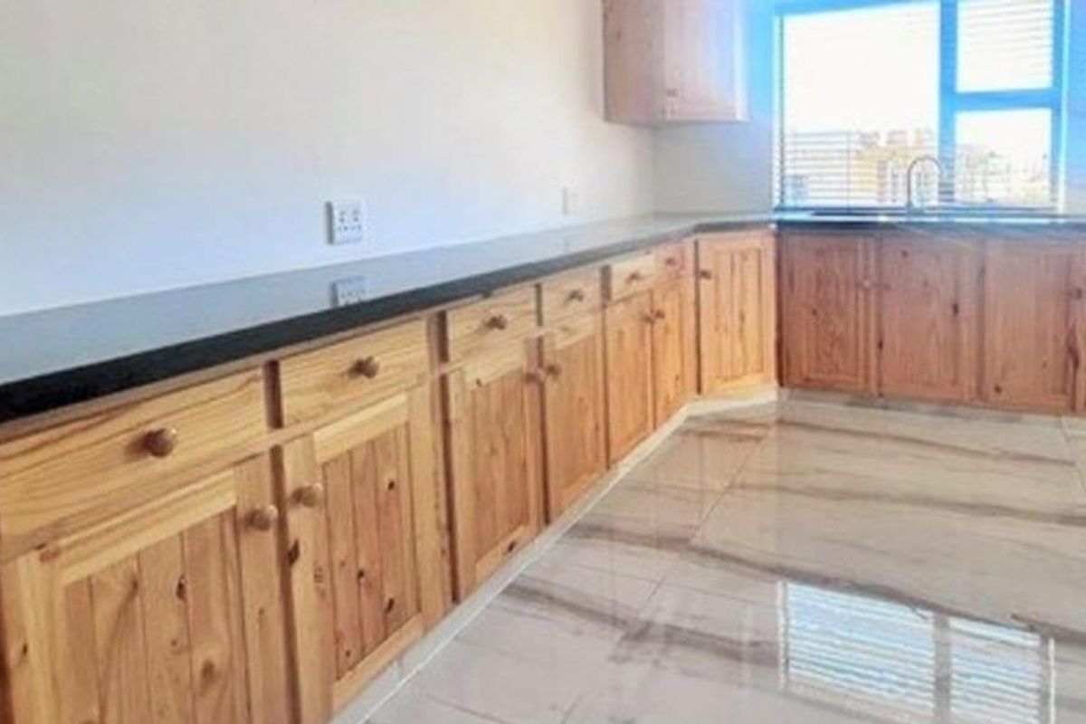 A functional kitchen featuring natural wood cabinetry, dark stone countertops, and polished light-toned floor tiles with a window above the sink area.