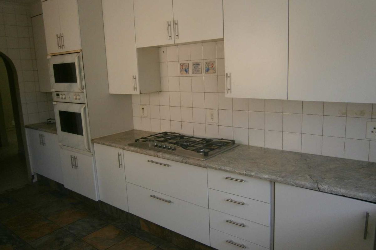 A functional kitchen featuring white cabinetry, stone-look laminate countertops, a built-in gas hob, and a wall-mounted oven, finished with tiled flooring.