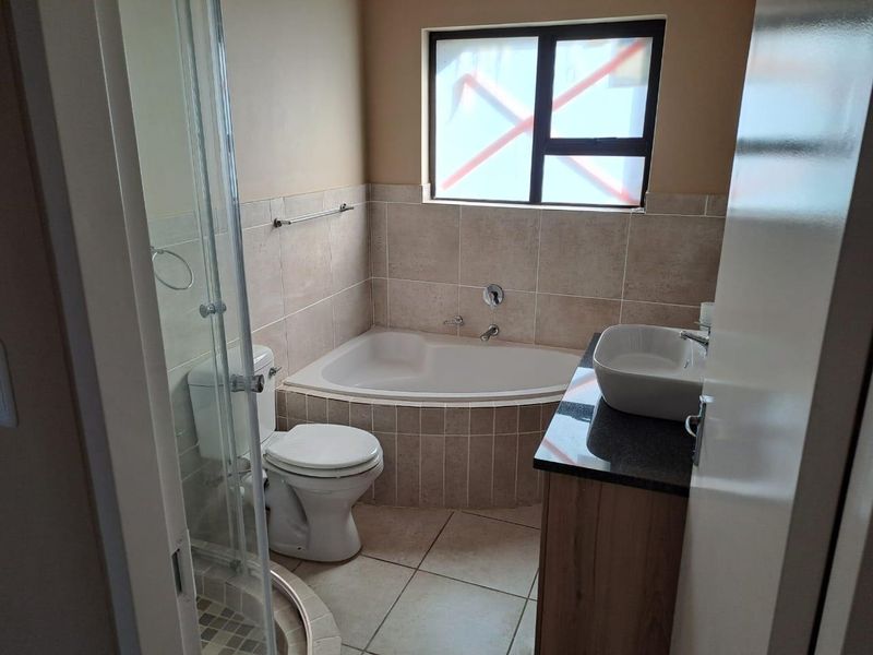 A functional bathroom featuring a corner bathtub, glass shower enclosure, vanity with vessel sink, and neutral tiled finishes.