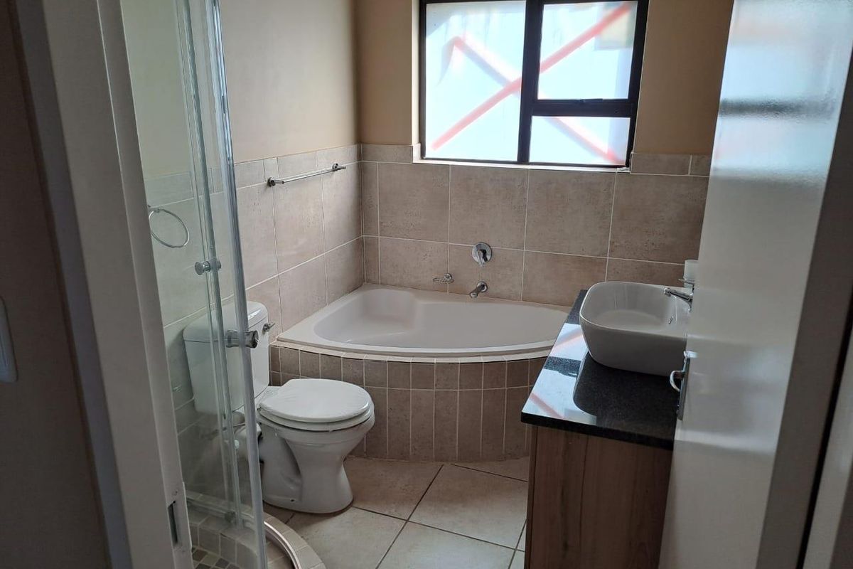 A functional bathroom featuring a corner bathtub, glass shower enclosure, vanity with vessel sink, and neutral tiled finishes.