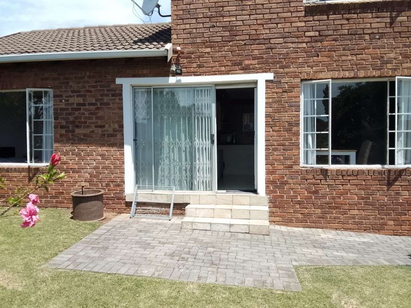 Rear exterior view of the townhouse featuring a brick facade, paved patio area, and sliding door access to the interior living space.