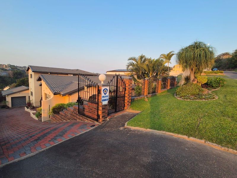 Front exterior view of the property featuring a paved driveway, secure wrought iron gated entrance, brick boundary wall, and well-maintained garden.