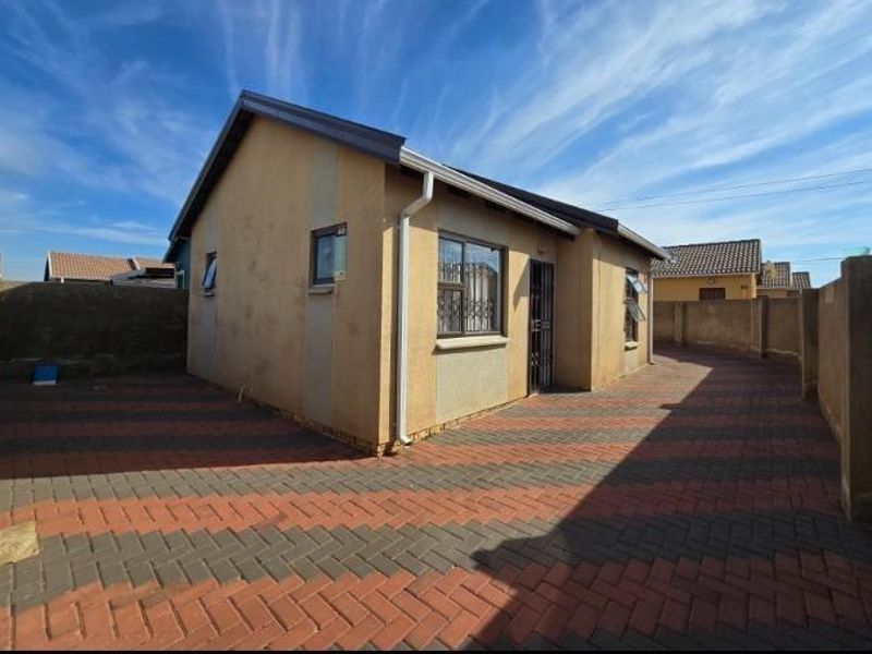 A well-maintained single-story house featuring a paved driveway, secure perimeter walling, and modern aluminium window frames.