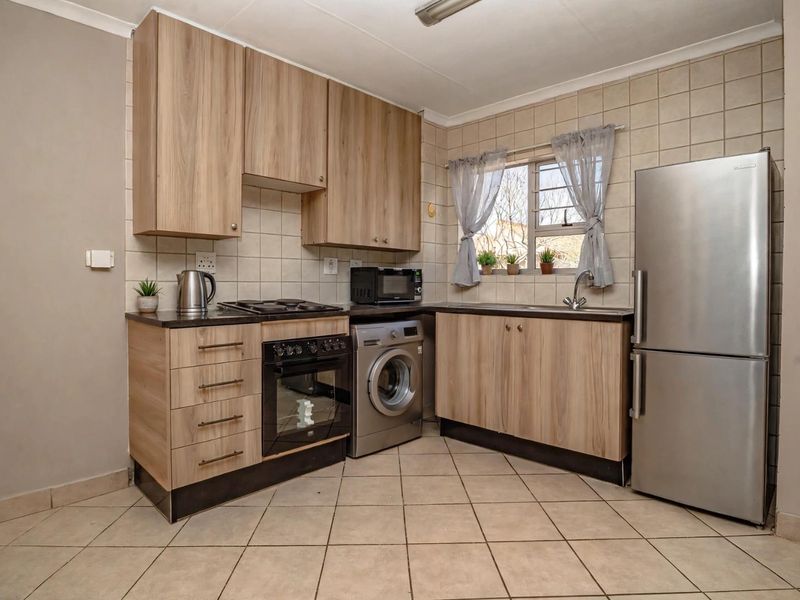 A functional kitchen featuring light wood-look cabinetry, tiled backsplash, built-in oven with gas hob, and dedicated space for a washing machine.