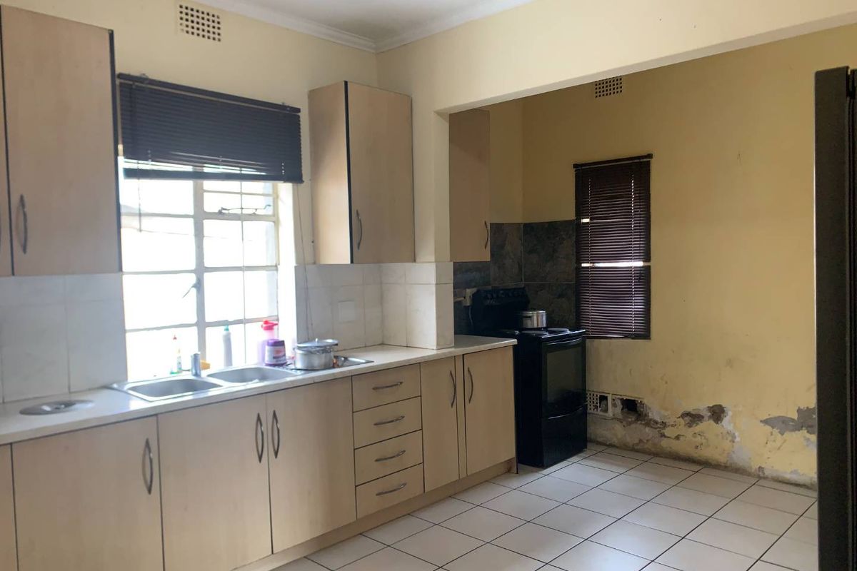 A dated kitchen featuring light wood cabinetry, tiled flooring, and a double sink, requiring cosmetic updates and wall repairs.