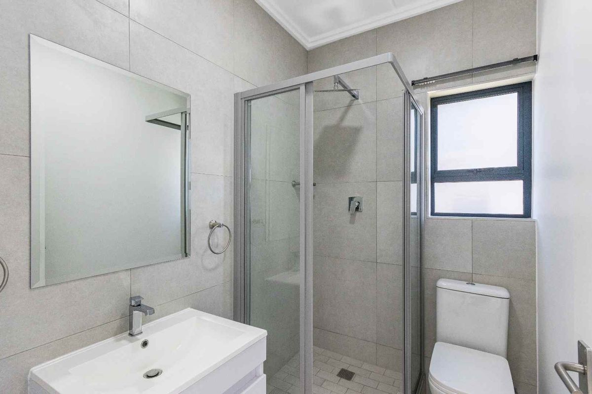 Modern bathroom featuring a glass shower enclosure, vanity basin, wall-mounted mirror, and neutral floor-to-ceiling tiling.