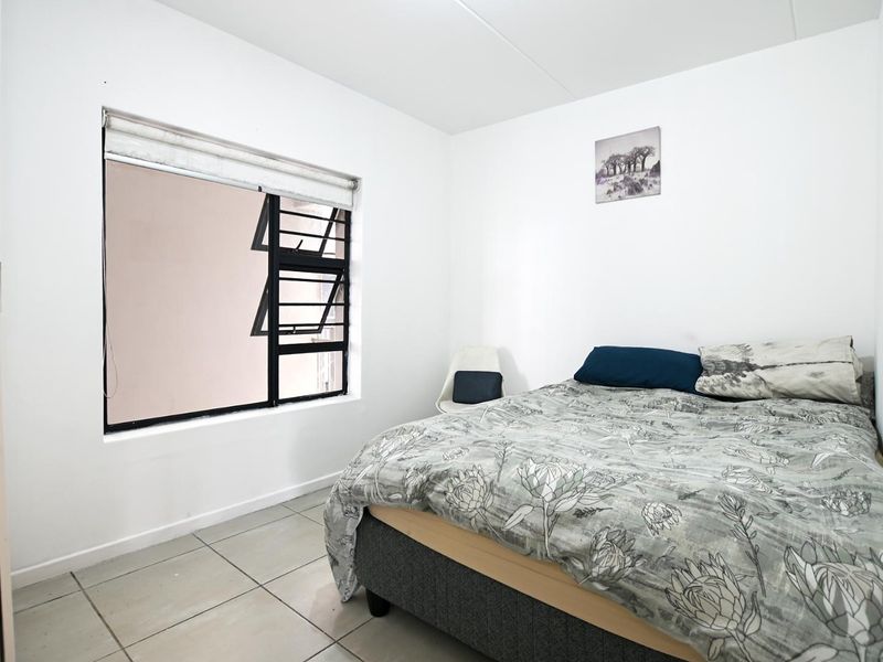 A functional bedroom featuring tiled flooring and a window fitted with security bars and a roller blind.