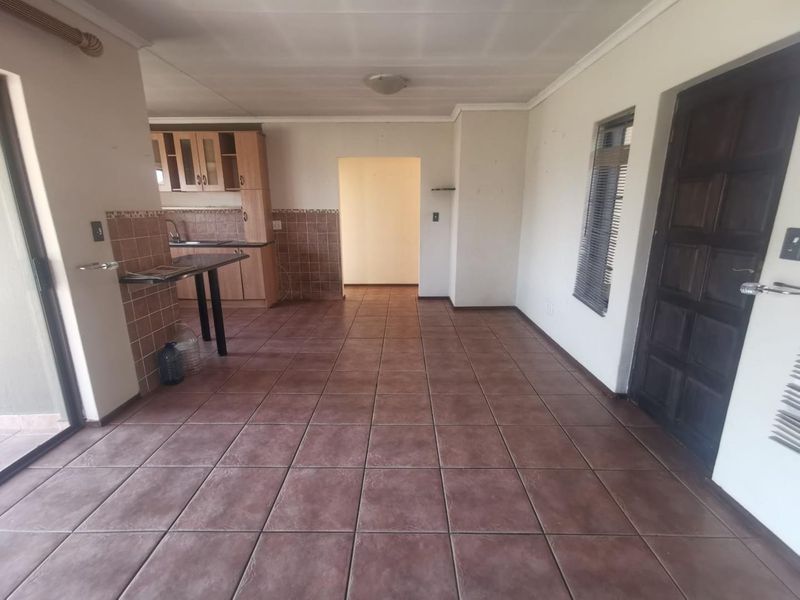 An open-plan living and kitchen area featuring tiled flooring, built-in cabinetry with a breakfast bar, and direct access to the exterior.