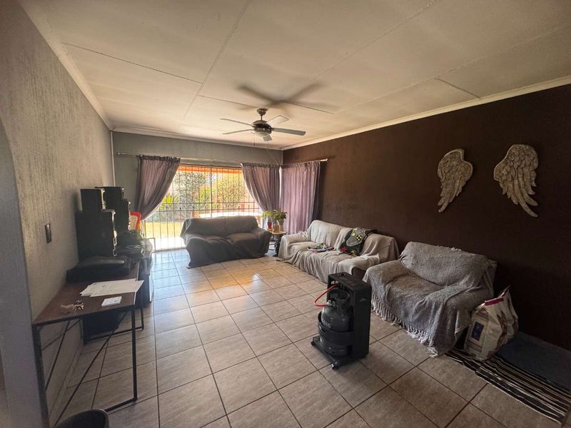 A spacious living room featuring tiled flooring, a ceiling fan, and a sliding glass door leading to the exterior.