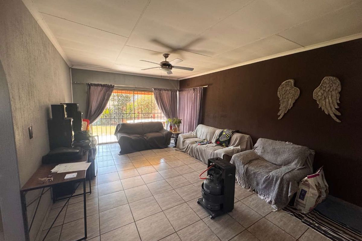 A spacious living room featuring tiled flooring, a ceiling fan, and a sliding glass door leading to the exterior.