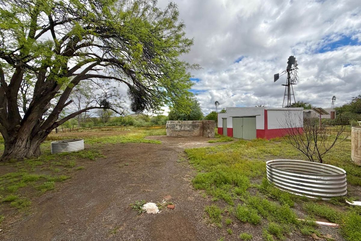 Outdoor area featuring a windmill, water storage tanks, and a small outbuilding set within a rural landscape.