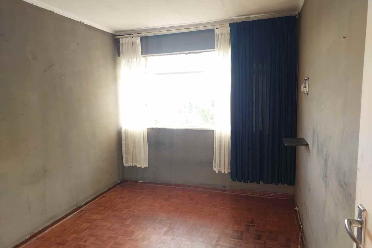 An empty bedroom featuring parquet flooring and unfinished wall surfaces, offering a blank canvas for renovation and interior design updates.