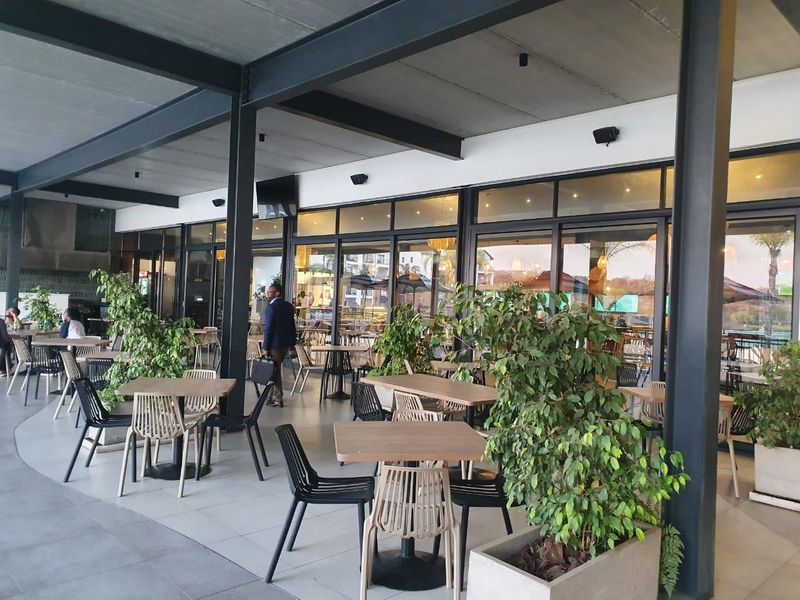 A spacious covered patio area featuring modern industrial steel structural elements, large glass sliding doors, and tiled flooring, suitable for outdoor dining.