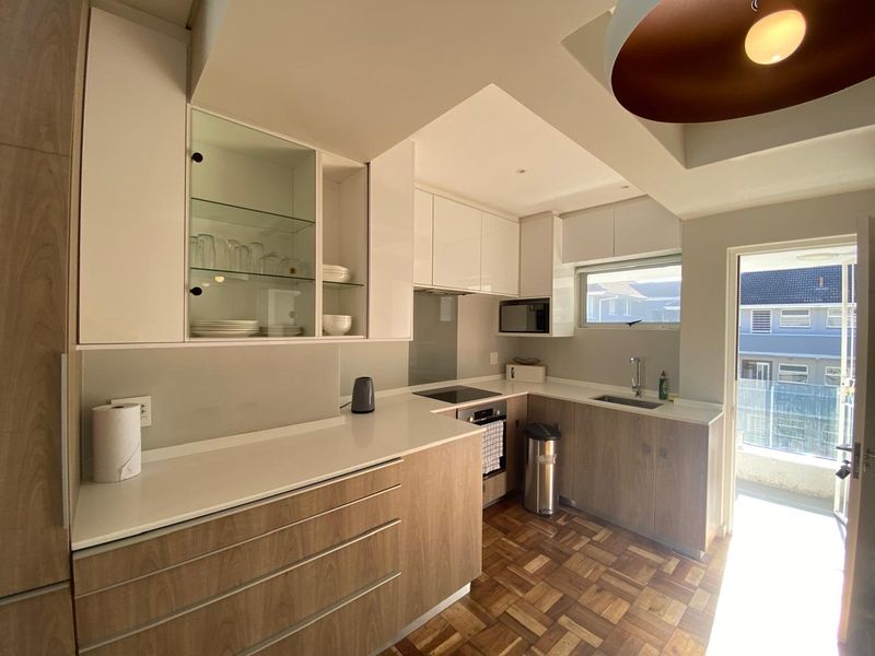 Modern kitchen featuring wood-tone lower cabinetry, white upper cabinets, stone countertops, integrated appliances, and classic parquet flooring with direct access to a balcony.