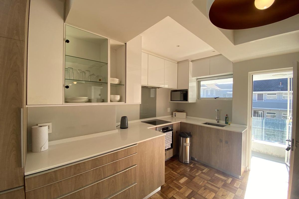 Modern kitchen featuring wood-tone lower cabinetry, white upper cabinets, stone countertops, integrated appliances, and classic parquet flooring with direct access to a balcony.
