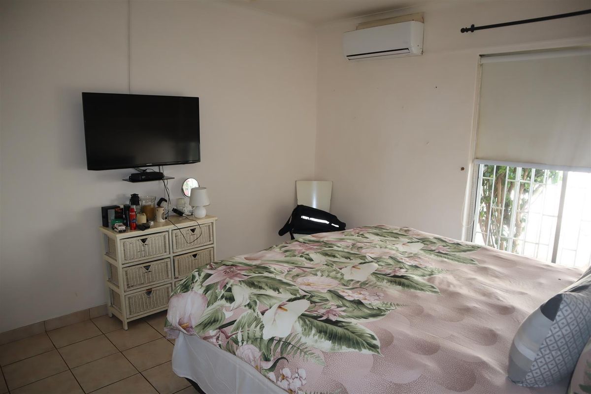 A functional bedroom featuring tiled flooring, a wall-mounted split-system air conditioner, and a window fitted with a roller blind.