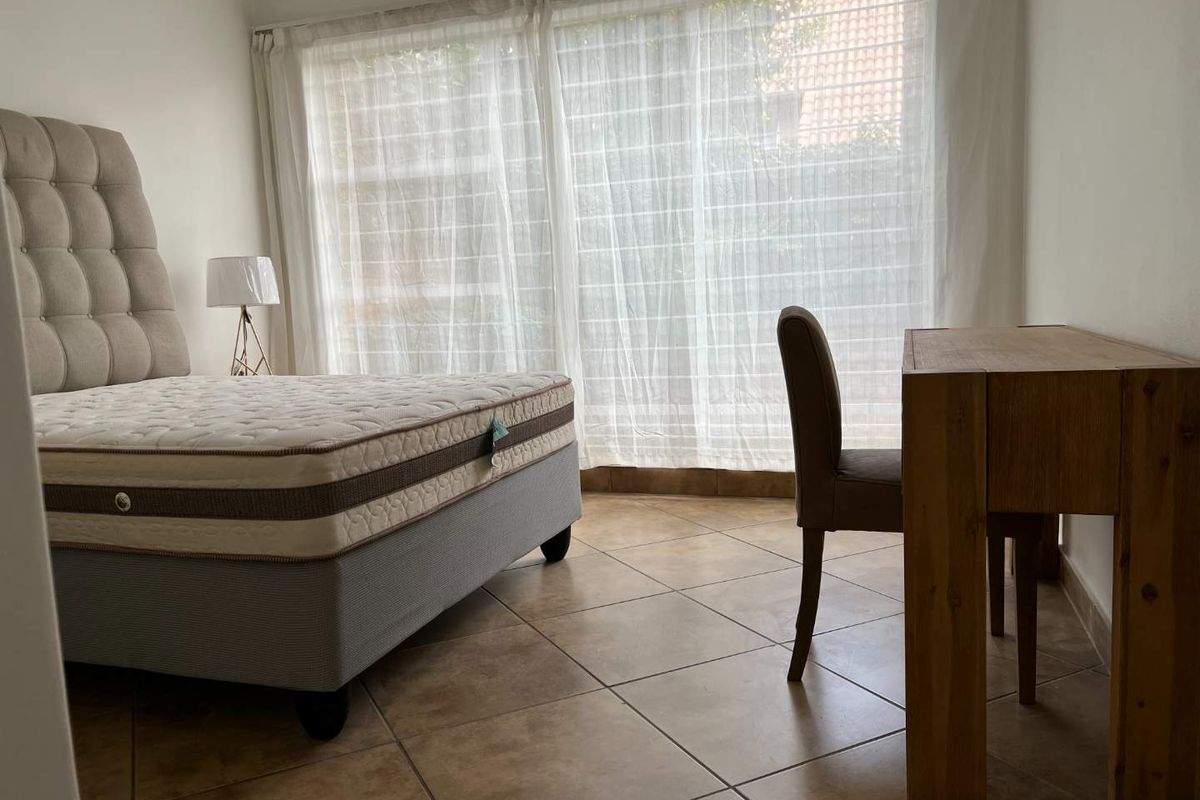 A bedroom featuring tiled flooring and a large window with sheer curtains, providing natural light.