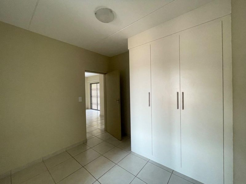 A clean, empty bedroom featuring neutral tiled flooring and white built-in cupboards, offering a versatile space ready for personalization.