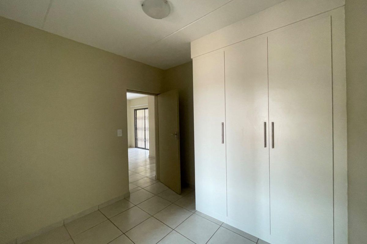 A clean, empty bedroom featuring neutral tiled flooring and white built-in cupboards, offering a versatile space ready for personalization.