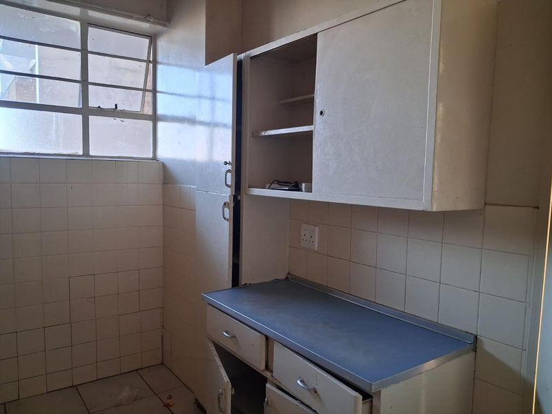 A dated kitchen area featuring original built-in cabinetry, tiled wall surfaces, and a steel window frame, requiring significant renovation and modernization.