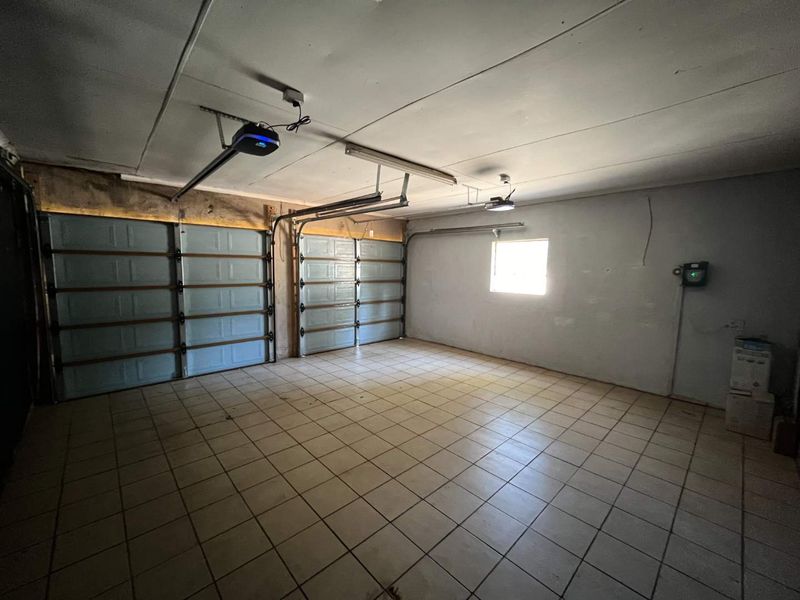 Spacious double garage featuring tiled flooring, automatic door openers, and a window, providing ample room for vehicle storage and utility use.