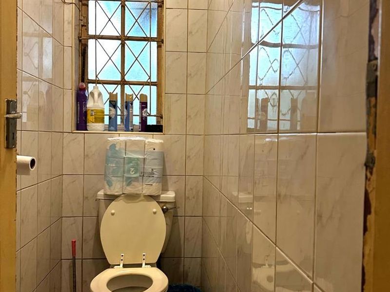 A compact bathroom featuring floor-to-ceiling wall tiles, a standard toilet, and a window with security bars.