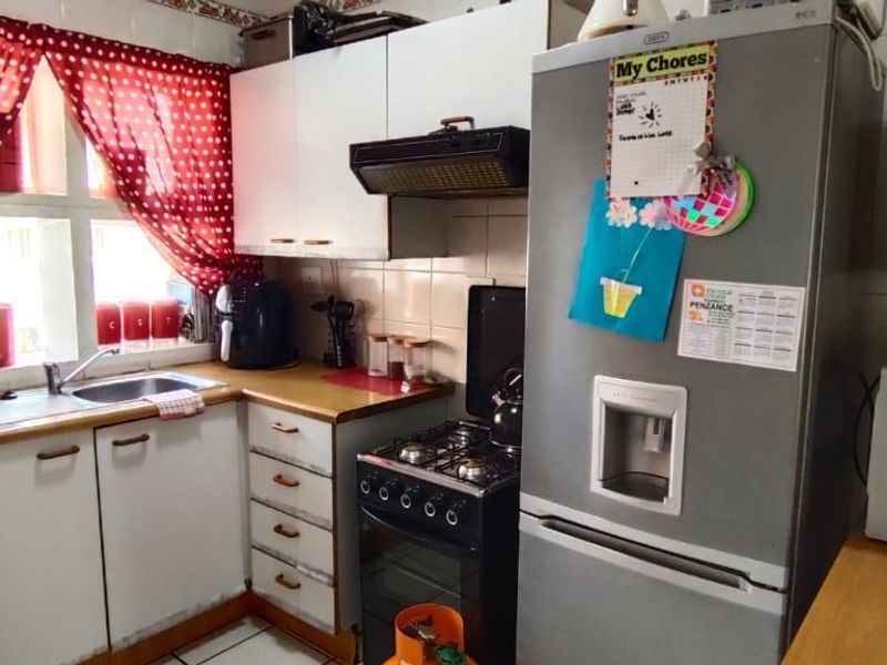 A functional kitchen featuring built-in cabinetry, a gas stove with extractor fan, and a stainless steel sink with tiled splashback.