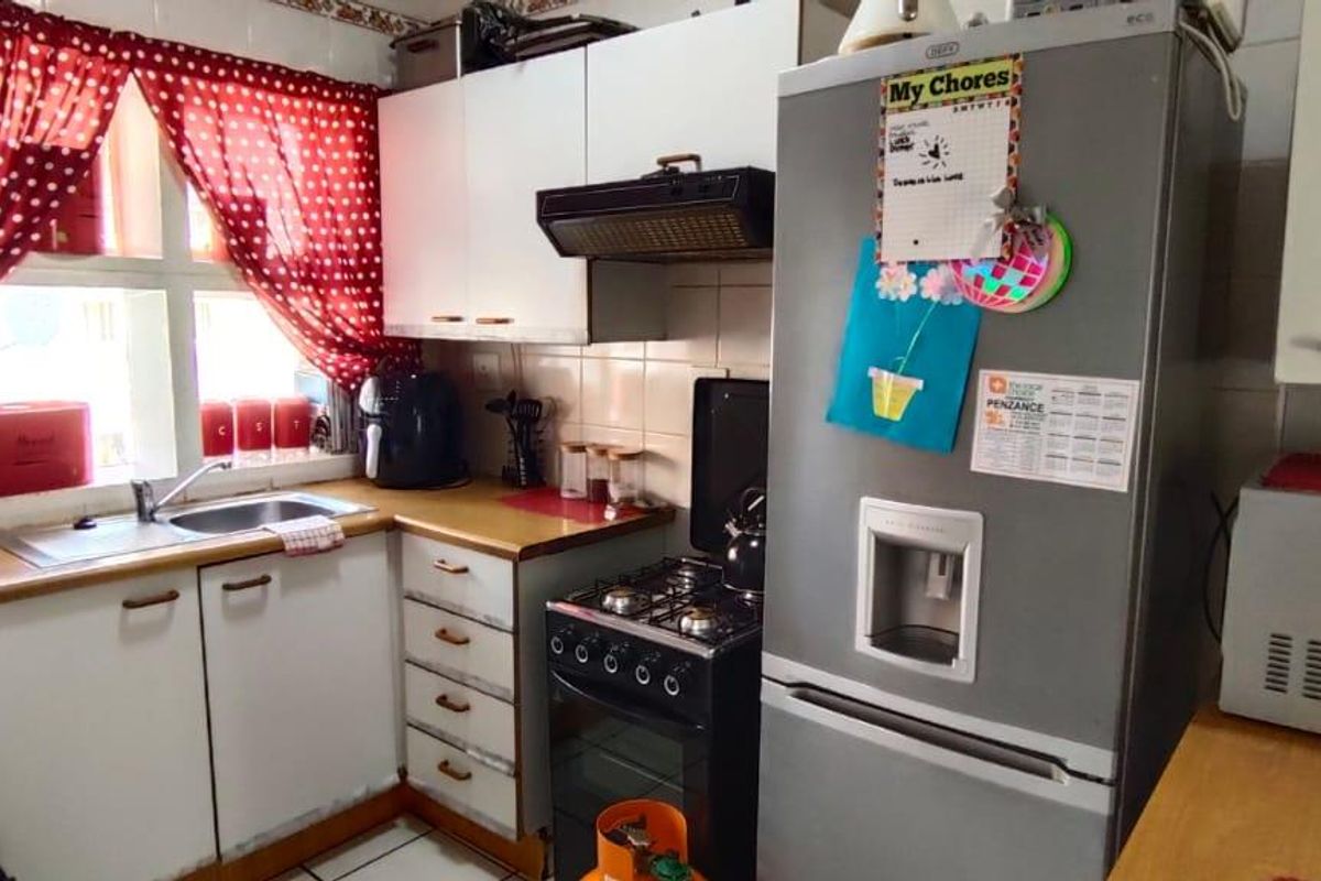 A functional kitchen featuring built-in cabinetry, a gas stove with extractor fan, and a stainless steel sink with tiled splashback.