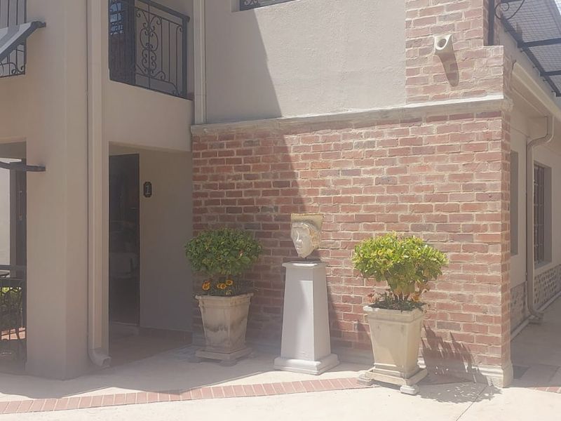 Front exterior view of the townhouse featuring a brick facade, wrought iron balcony detailing, and a paved driveway entrance.