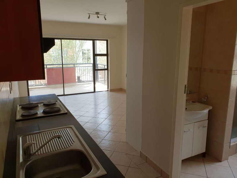 Open plan kitchen and living area featuring tiled floors, built-in hob, and direct access to a balcony, adjacent to a compact bathroom.