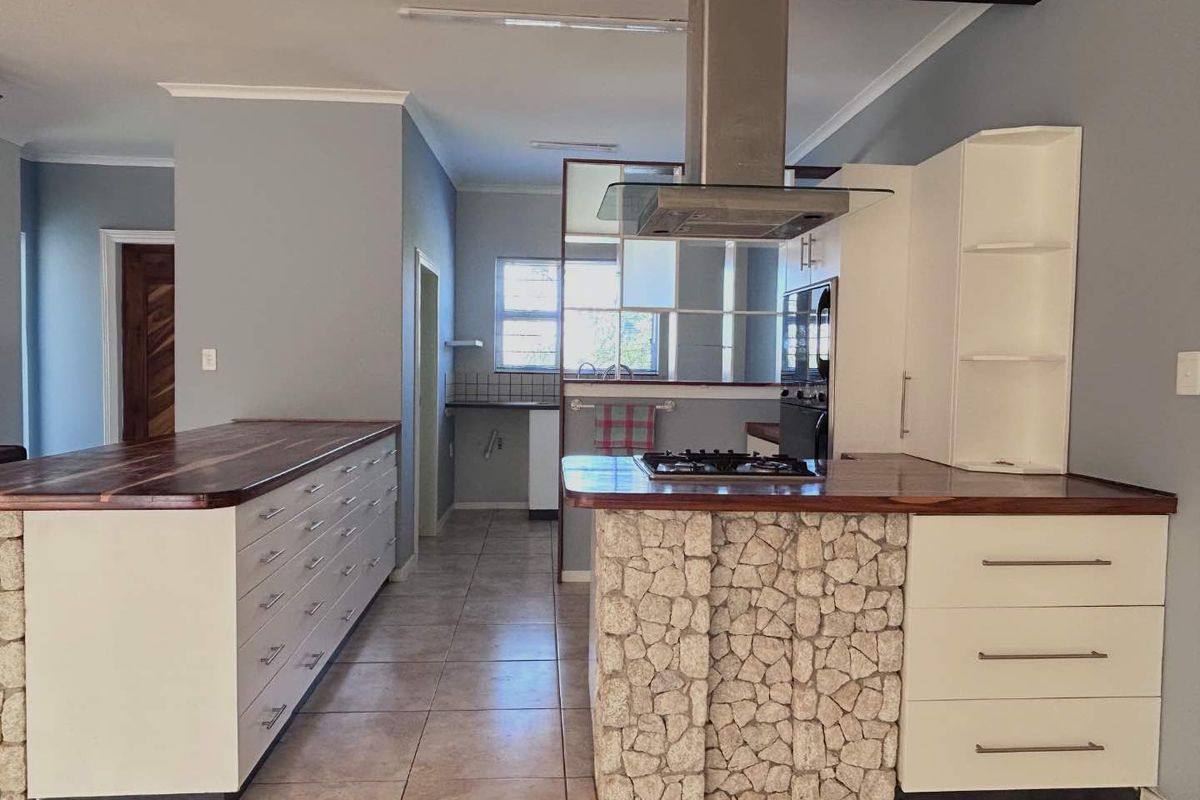 Modern kitchen featuring a stone-clad breakfast bar, wooden countertops, built-in gas hob, stainless steel extractor fan, and ample white cabinetry.