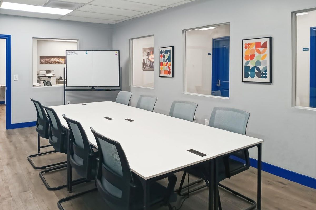 A modern, well-lit office meeting room featuring laminate flooring, internal glass partitions, and a professional conference setup with integrated power outlets.