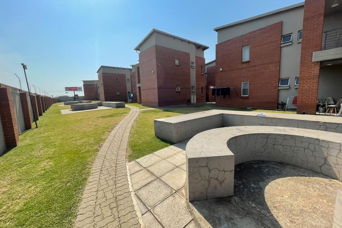 Communal outdoor area featuring paved walkways, manicured lawn, and built-in concrete seating between apartment blocks.
