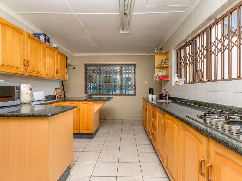 A functional kitchen featuring wooden cabinetry, granite countertops, a gas hob, and tiled flooring, offering a practical layout with ample storage space.