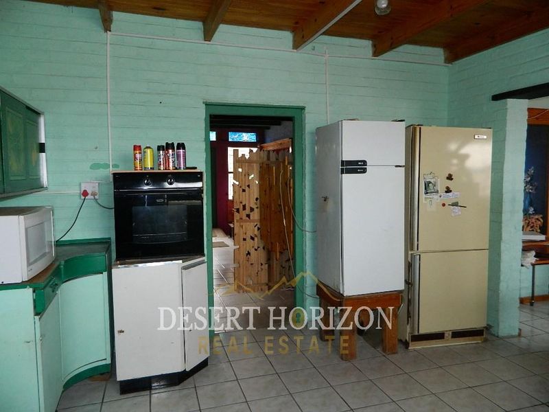 A dated kitchen featuring painted brick walls, exposed timber ceiling beams, tiled flooring, and a built-in oven, offering significant potential for modernization.