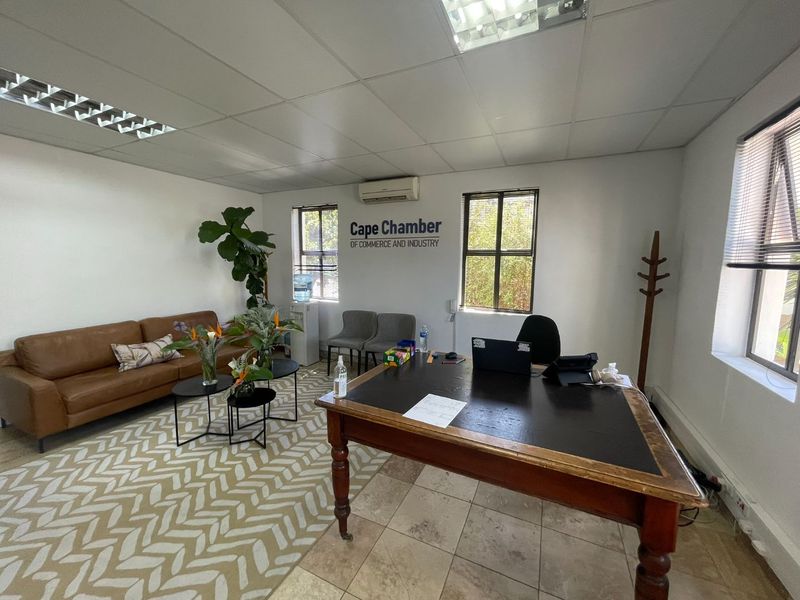 A functional office space featuring tiled flooring, suspended ceiling with recessed lighting, and a wall-mounted air conditioning unit.
